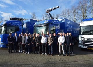 Teilnehmende der Abschlussveranstaltung stehen vor den Prototypen und einem dieselbetriebenen Referenzfahrzeug